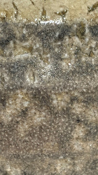 Macro detail of mottled ash glaze surface showing crystalline texture, mineral deposits, and the intentional interplay between grey and amber tones