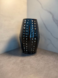 Side angle of a handmade black glazed ceramic vase with carved chevron screen work, showing blue-black glaze depth and sculptural surface texture