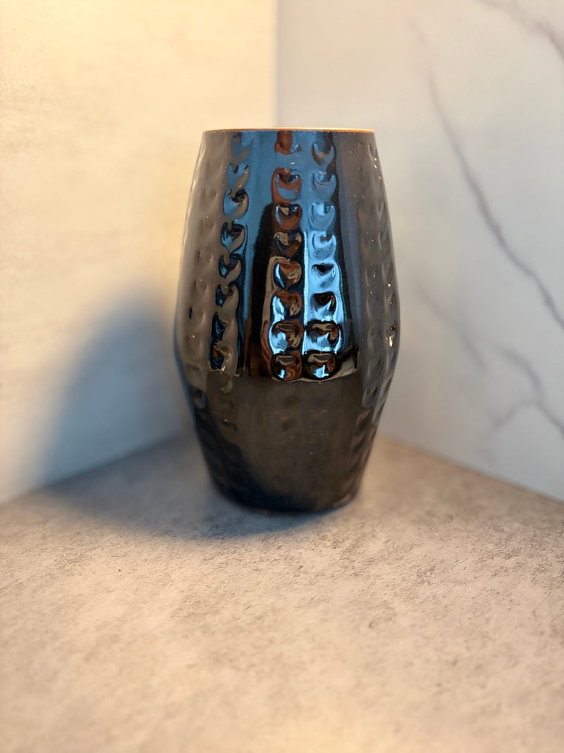 Front view of a handmade black glazed ceramic vase with carved chevron screen work pattern in vertical columns, photographed against a marble background