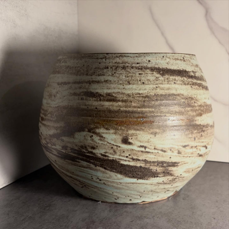 Sculptural round stoneware vessel with deliberate celadon and iron-oxide banded glaze surface, angled close-up view